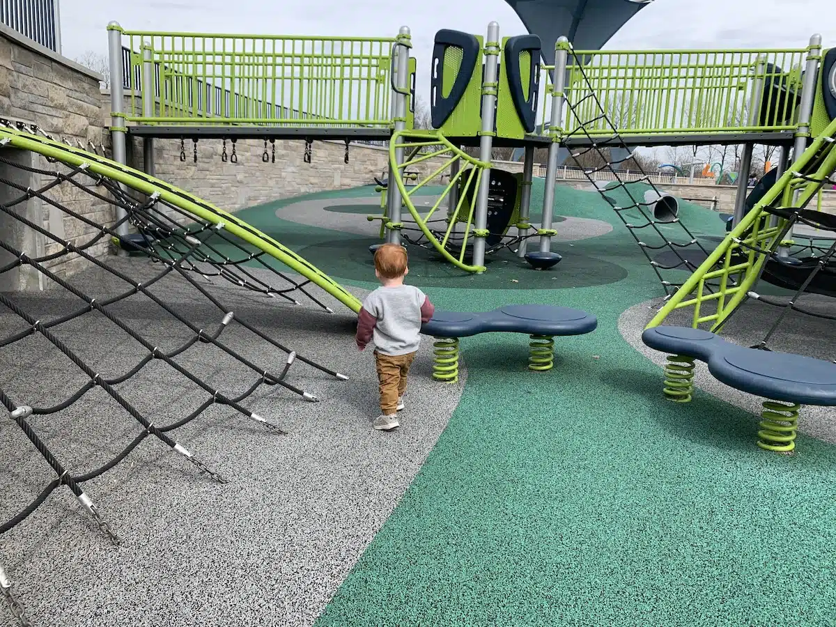 monkey bars under bridge, toddler boy on playground Full Shot of Why Westermeier Commons Is One of the Best Playgrounds in the Indy Area