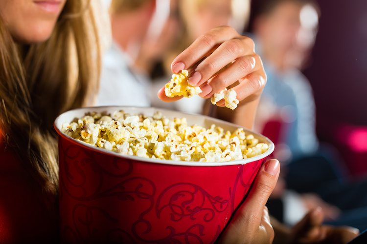Woman eating large container of popcorn in cinema or movie theater
