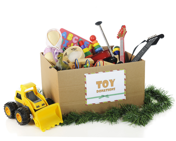 A large corrugated box with a "Toy Donations" sign. Its filled with assorted toys and surrounded by Christmas garland and a toy bulldozer. On a white background.