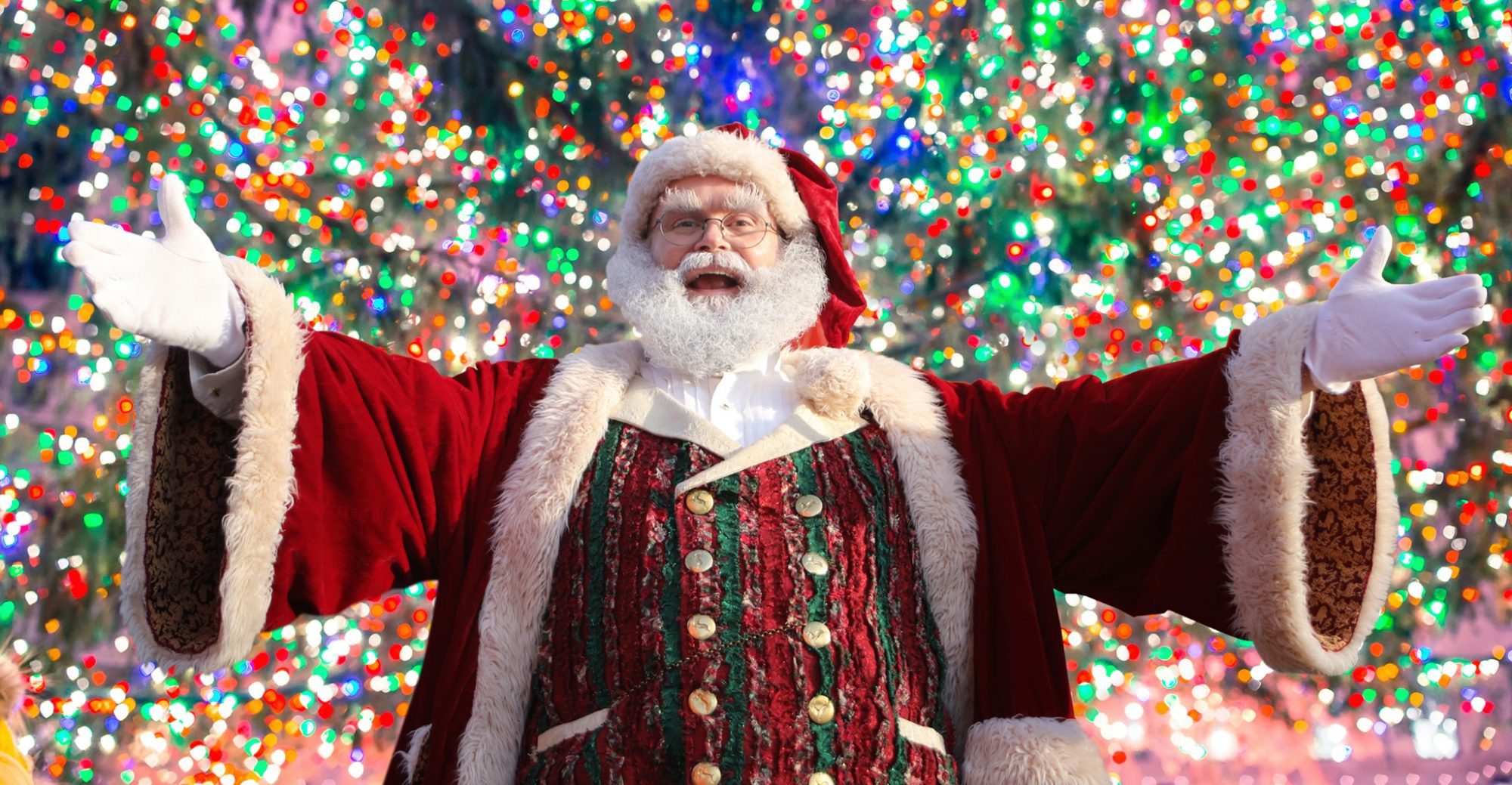 Santa in front of a wall of holiday lights