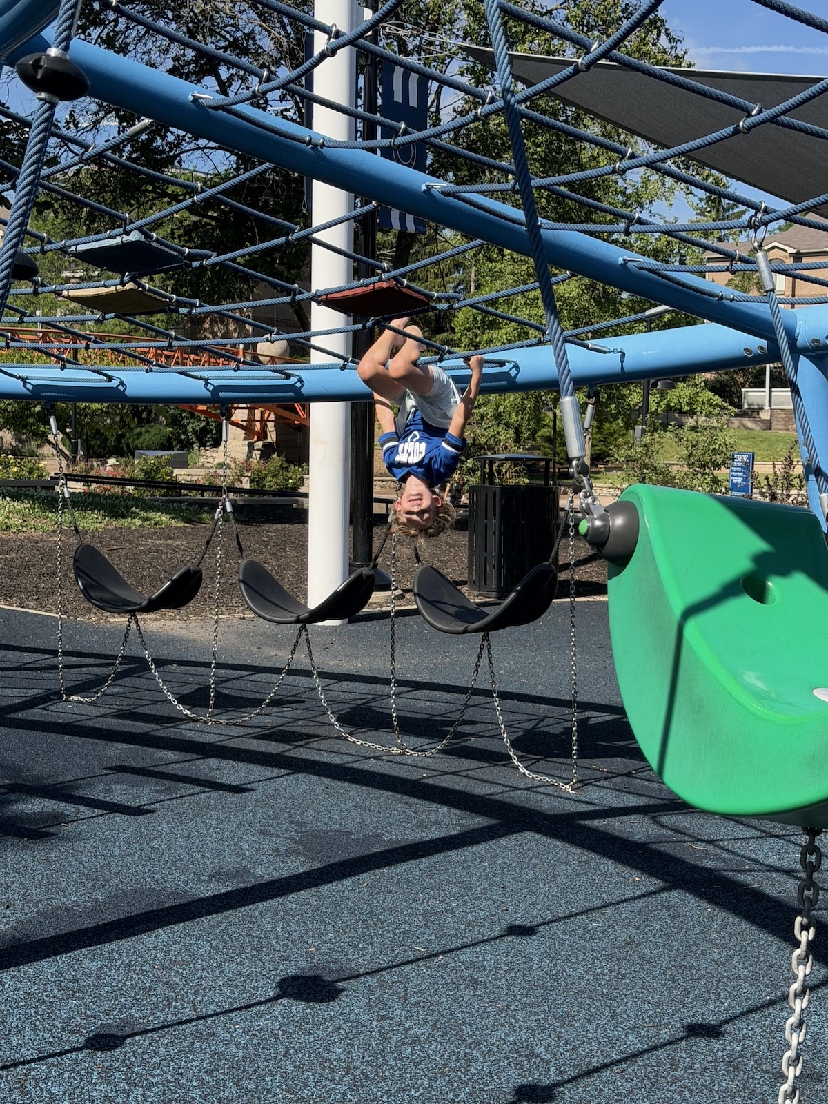 Child hanging upside down from the rope skywalk at Colts Canal Playground