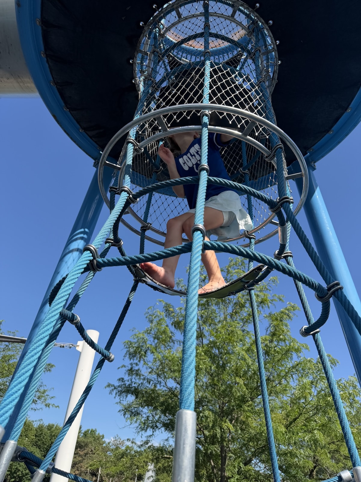 Child climbing the rope tower to reach the tall tube slide at Colts Canal Playground