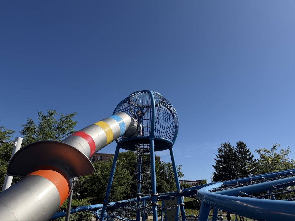 Child at the top of the blue climbing tower at Colts Canal Playground in downtown Indianapolis