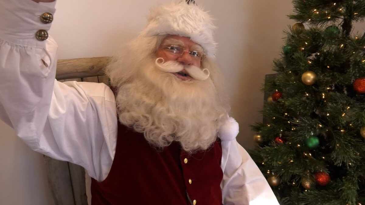 Santa waving beside a Christmas tree in his Whitestown workshop