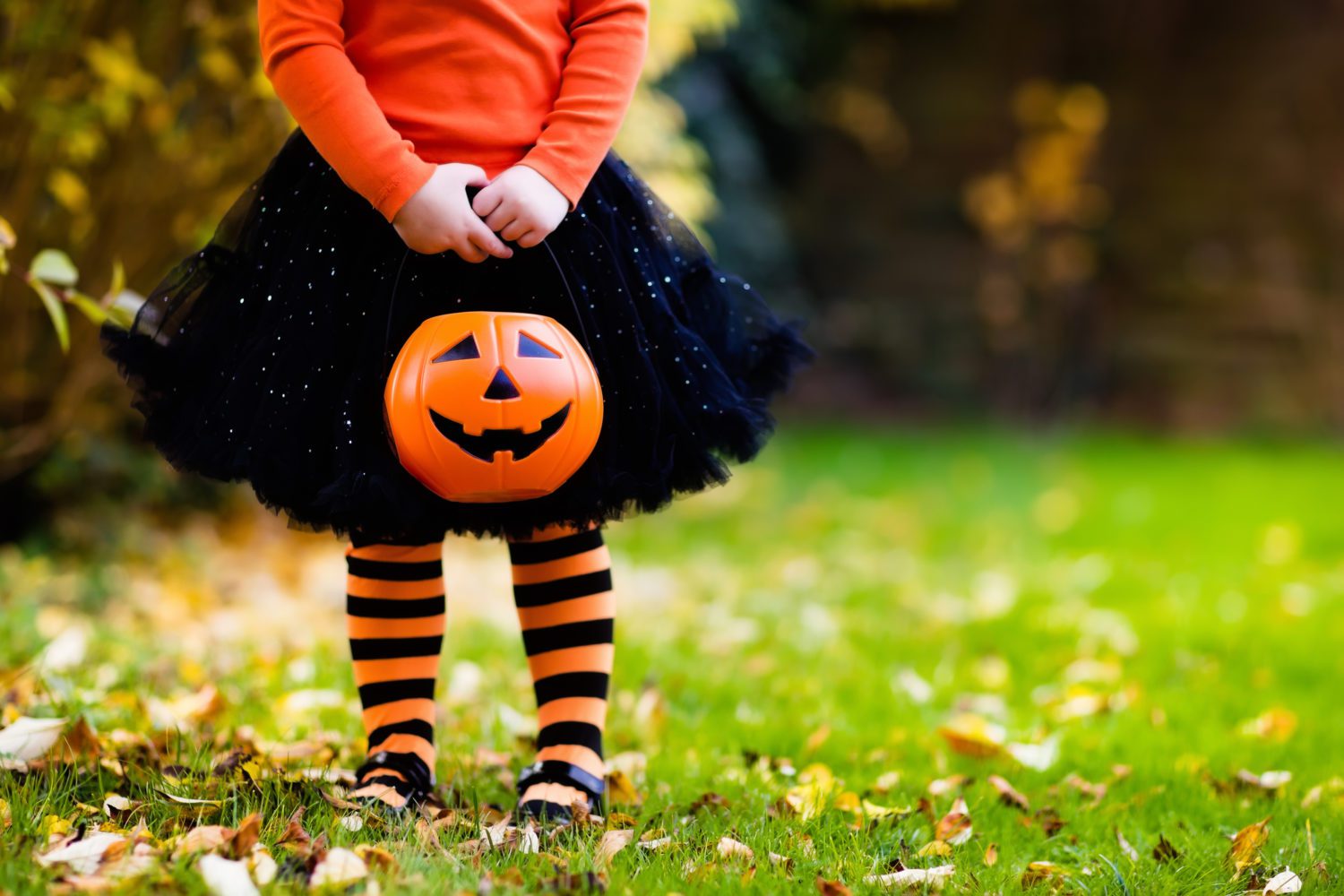 A child in a Halloween costume holding a jack-o'-lantern bucket