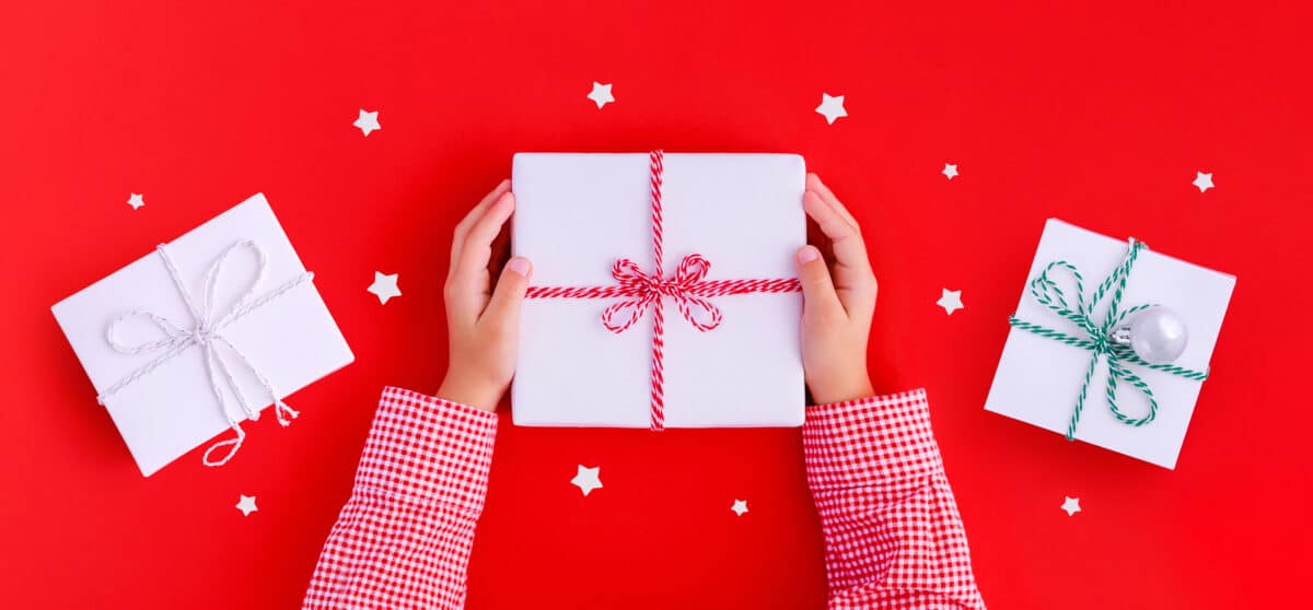 Child's hands holding a wrapped gift box on a red background