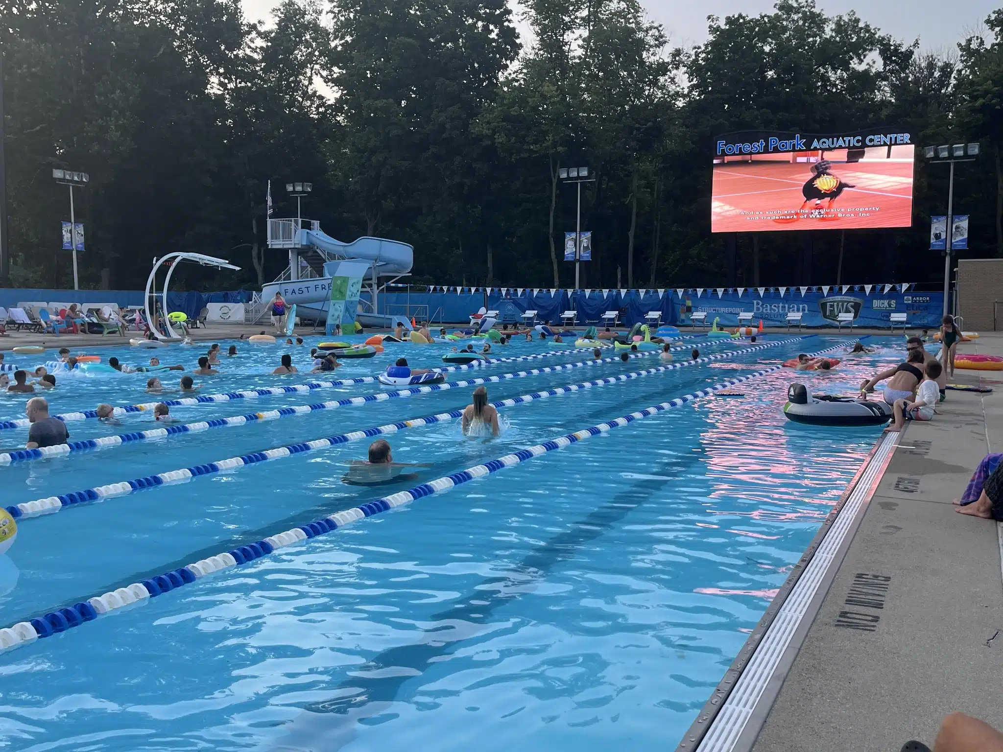 Movie screen lit up at dusk over the pool during Flix and Floats at Forest Park Aquatic Center in Noblesville