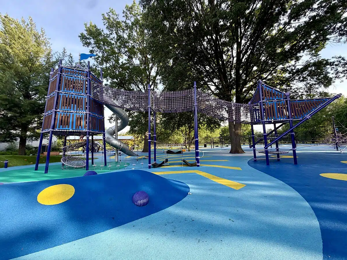 Wide view of Frederick Douglass Playground with tall climbing towers and an enclosed rope bridge