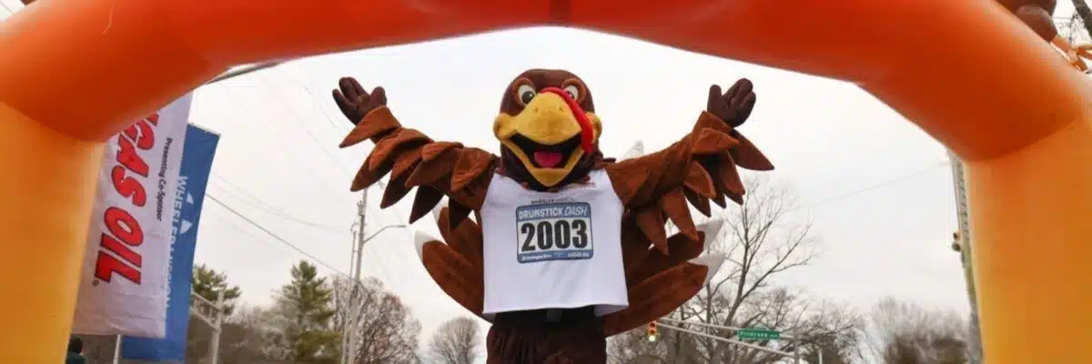 The Drumstick Dash turkey mascot spreads its wings under the orange finish-line arch