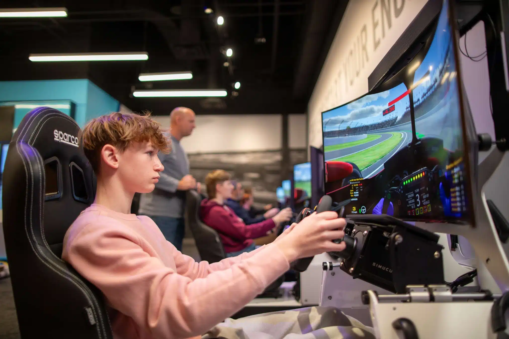 A boy grips the wheel of a racing simulator facing a curved screen that shows the track at the Indianapolis Motor Speedway Museum