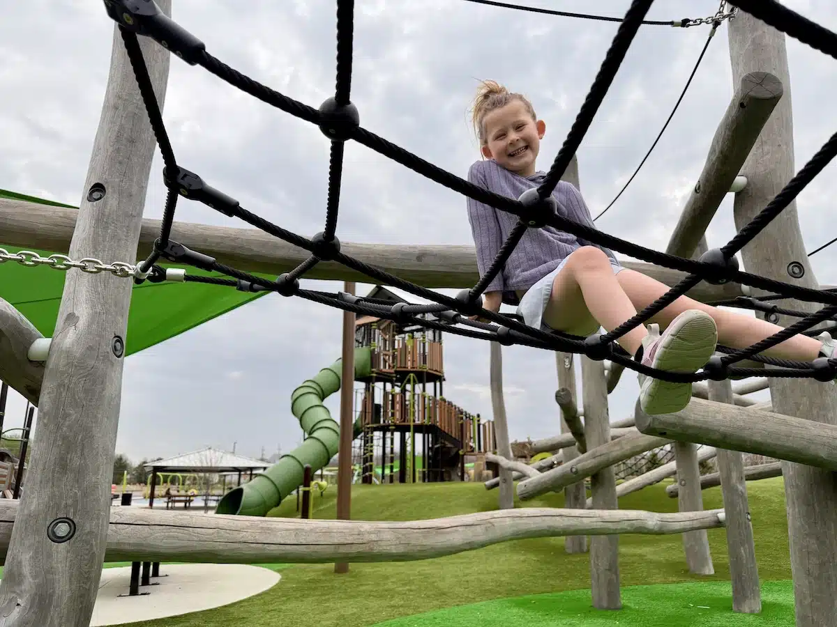 Young girl climbing the wooden nature obstacle course with rope bridges and log posts at Grassy Creek Park playground