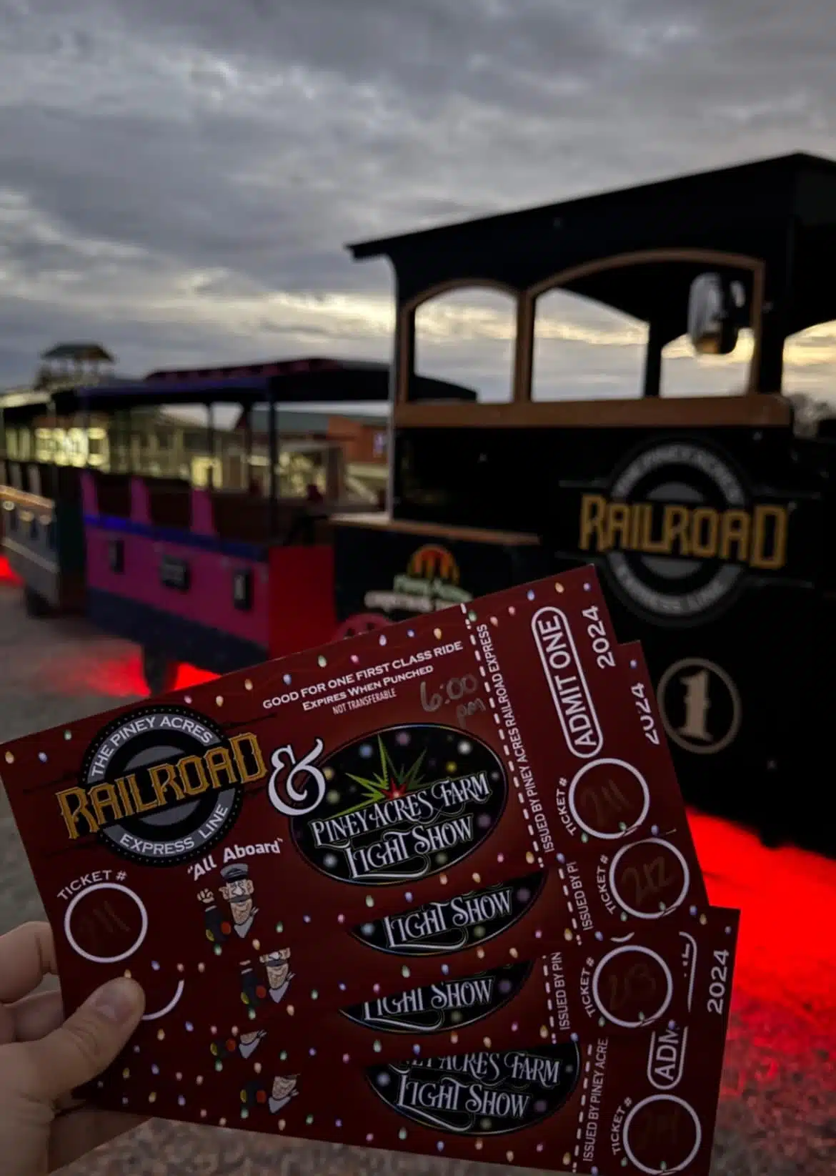 Child holding Piney Acres Express tickets for the Glimmer Lights holiday train ride at Piney Acres Farm