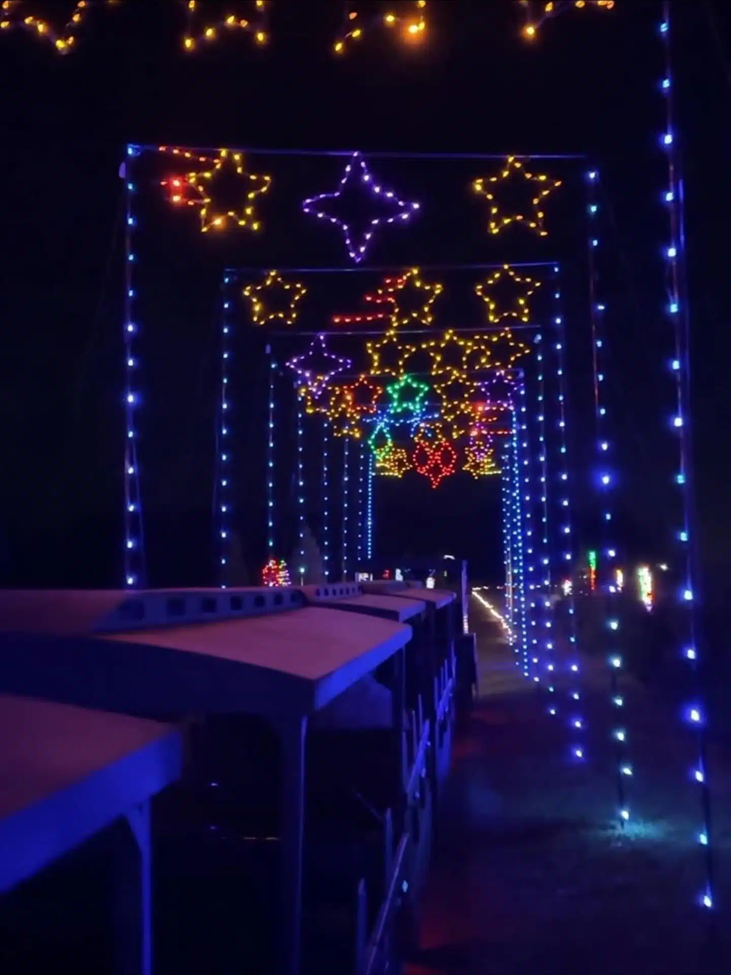 Glimmer Lights at Piney Acres: Train Rides, Santa and Holiday Lights 4 The Piney Acres Express holiday train passing under colorful light displays at night during Glimmer Lights at Piney Acres Farm