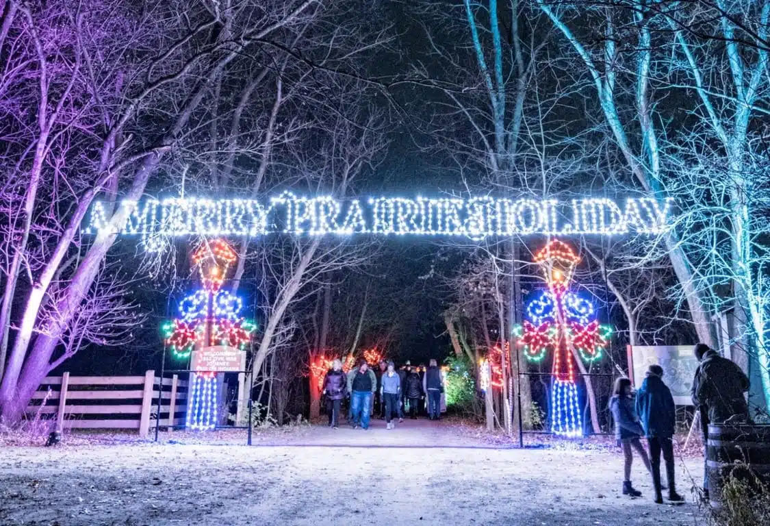 Best Christmas Lights in Indianapolis 2026 6 Families walking lantern-lit streets at A Merry Prairie Holiday at Conner Prairie in Fishers