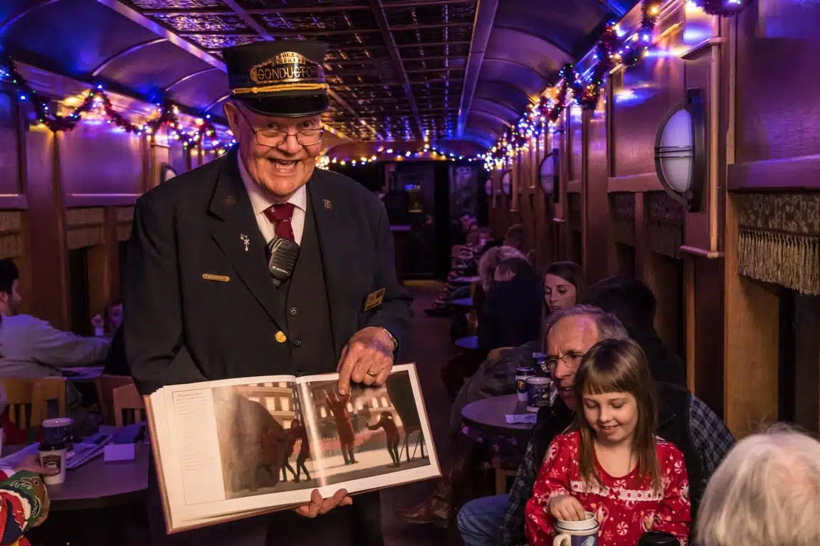 Conductor showing a picture book to families in a decorated train car on the Polar Express train ride in French Lick