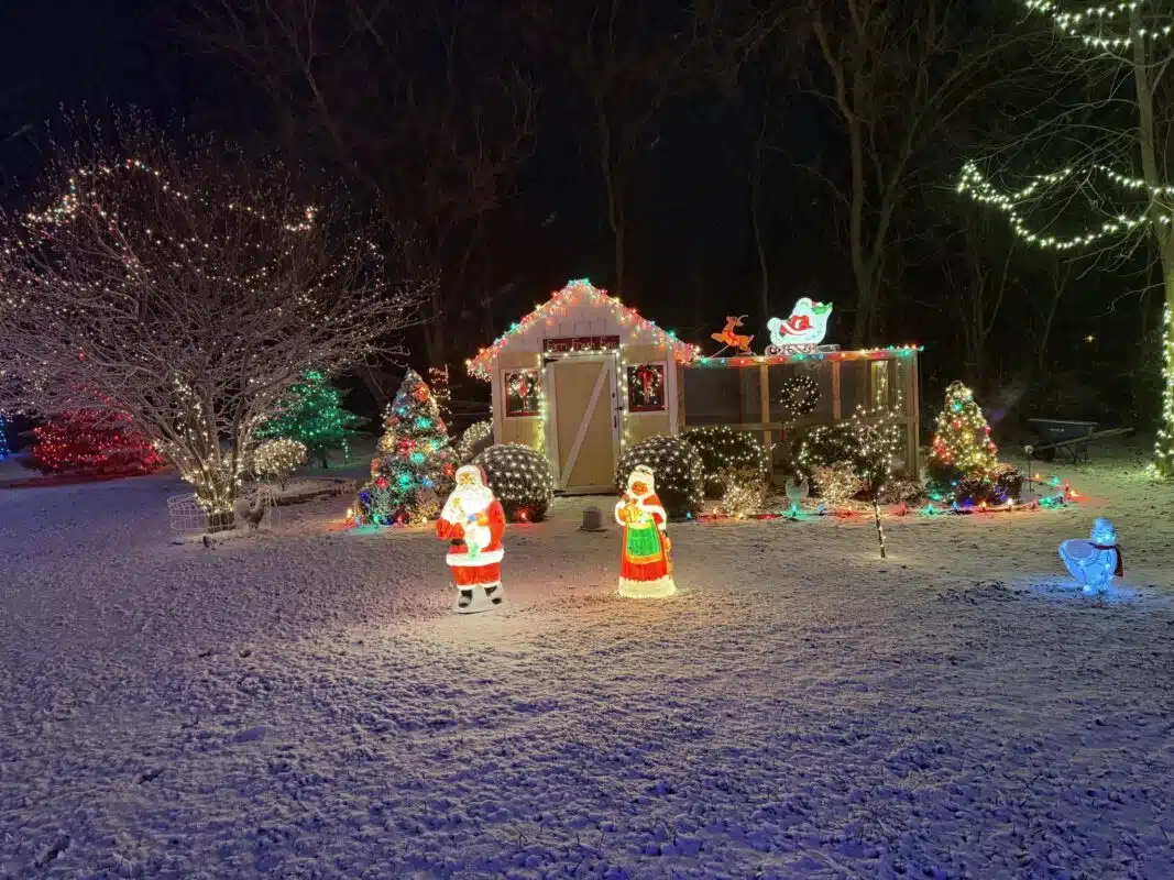 A lit-up cottage, Santa and holiday figures in the snow at Christmas Acres