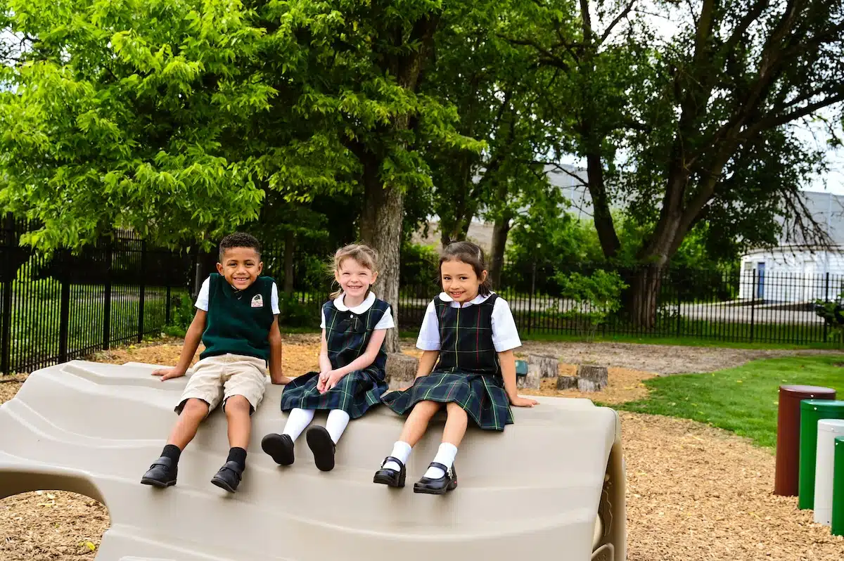 Pre-K students sitting together on a climbing log at recess at The Oaks Academy Early Education Center