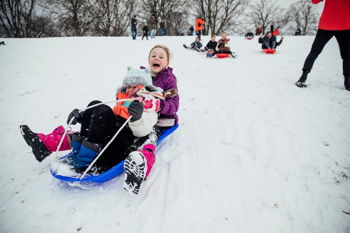 Kids racing down snowy sledding hill at Indianapolis area park