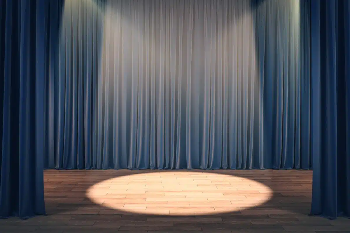 A spotlight on a stage in front of blue theater curtains