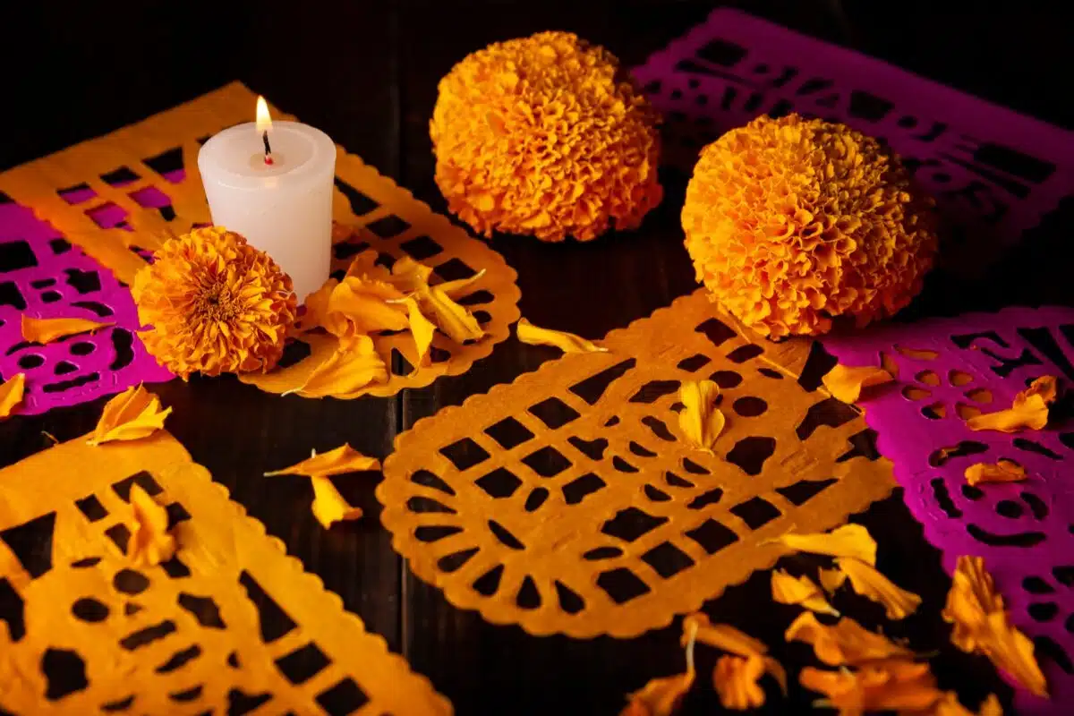 A candle with marigolds and orange papel picado for Día de los Muertos