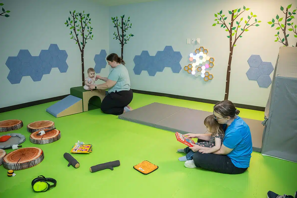 Conner Prairie Guide 2026: Tickets, Hours and What Kids Do 2 Caregivers and young children play on soft mats and log stools in the Sensory Room at the Conner Prairie Museum Experience Center