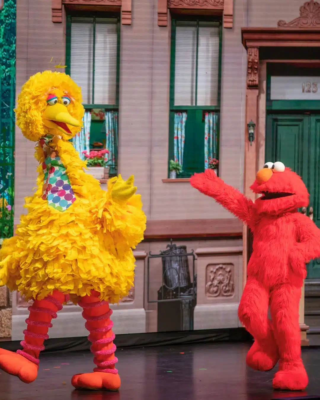 Big Bird and Elmo dancing in front of the 123 Sesame Street brownstone on stage