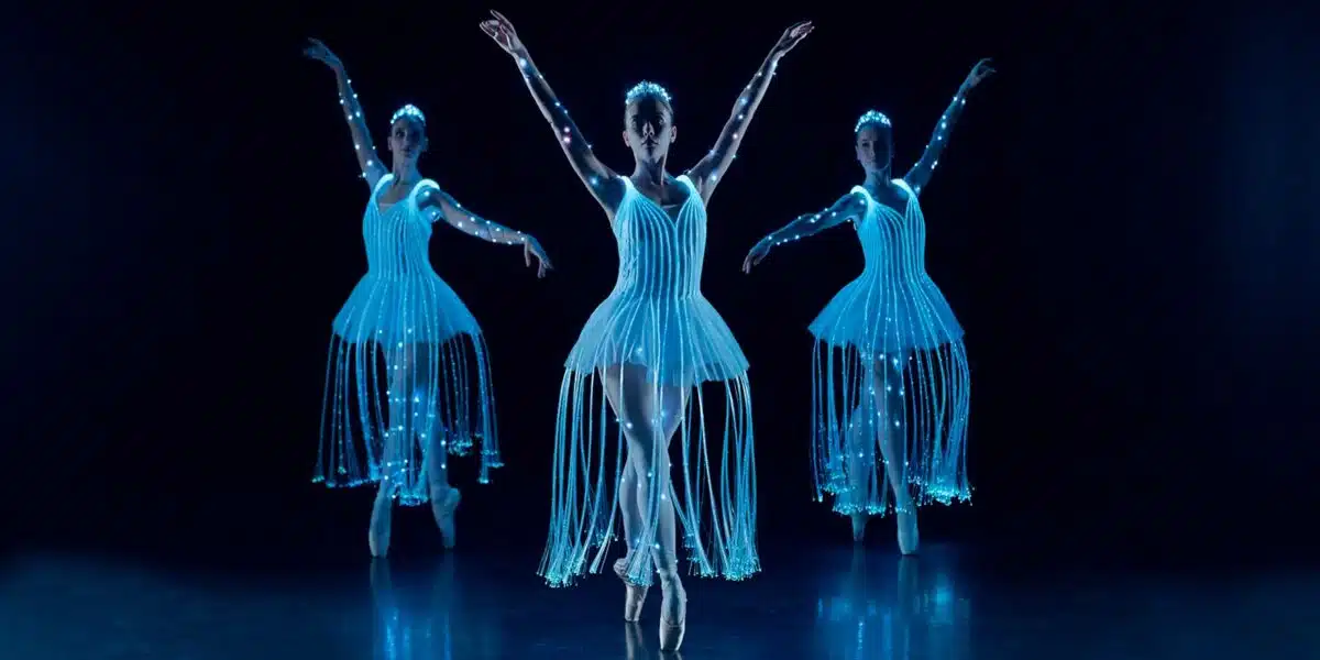 Three ballet dancers in illuminated costumes on a dark stage
