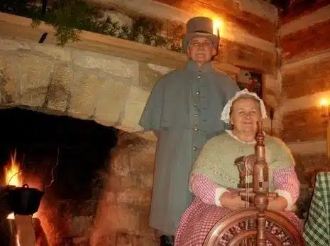 Costumed interpreters beside a cabin fireplace during Holiday in the Village at Spring Mill State Park